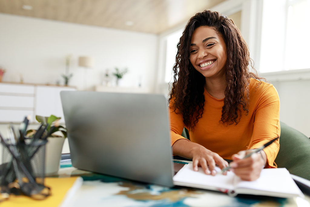 Woman sitting at desk, using computer and writing in notebook Theory & Practice of Mediation