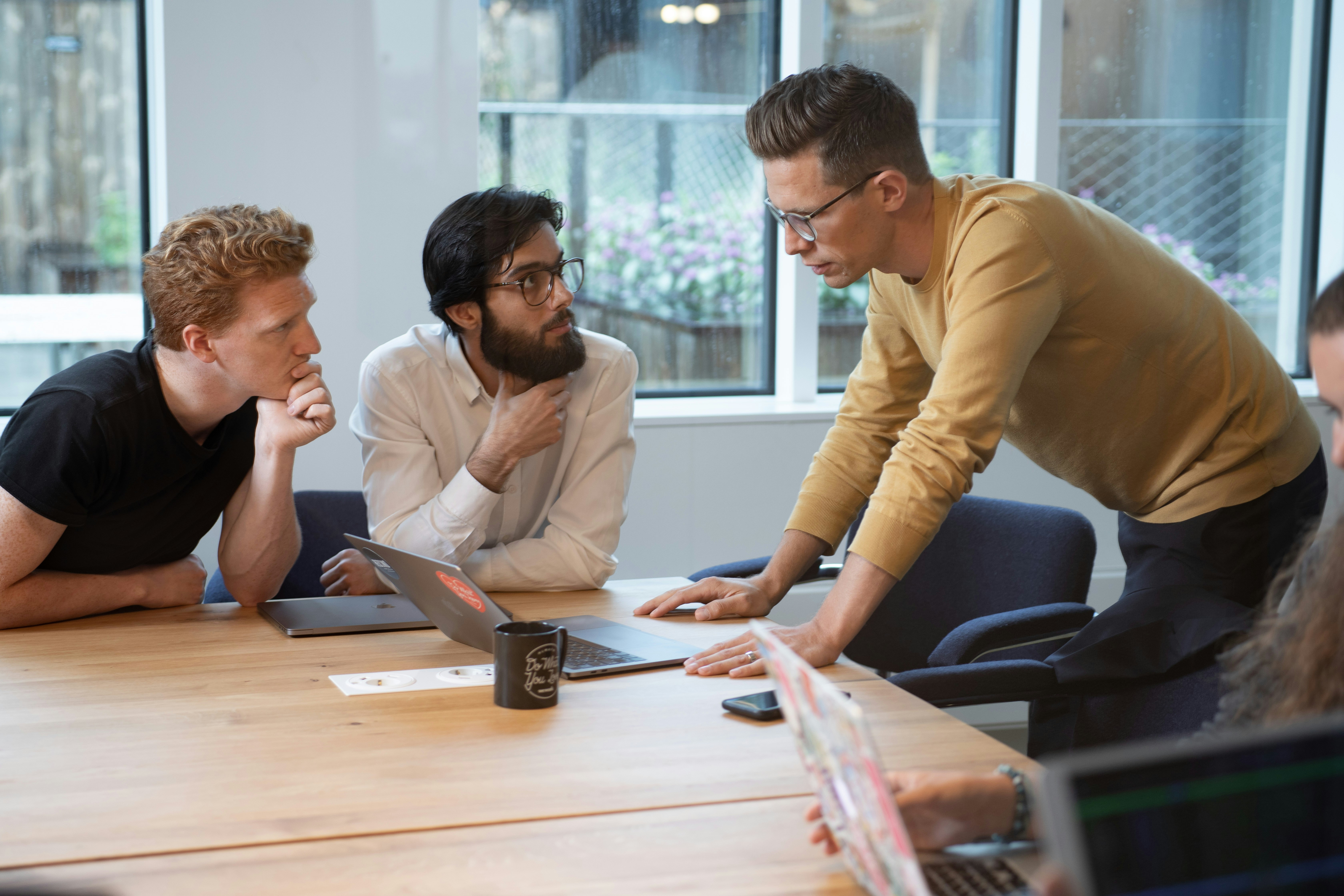 Three men having a discussion at a table with a laptop.