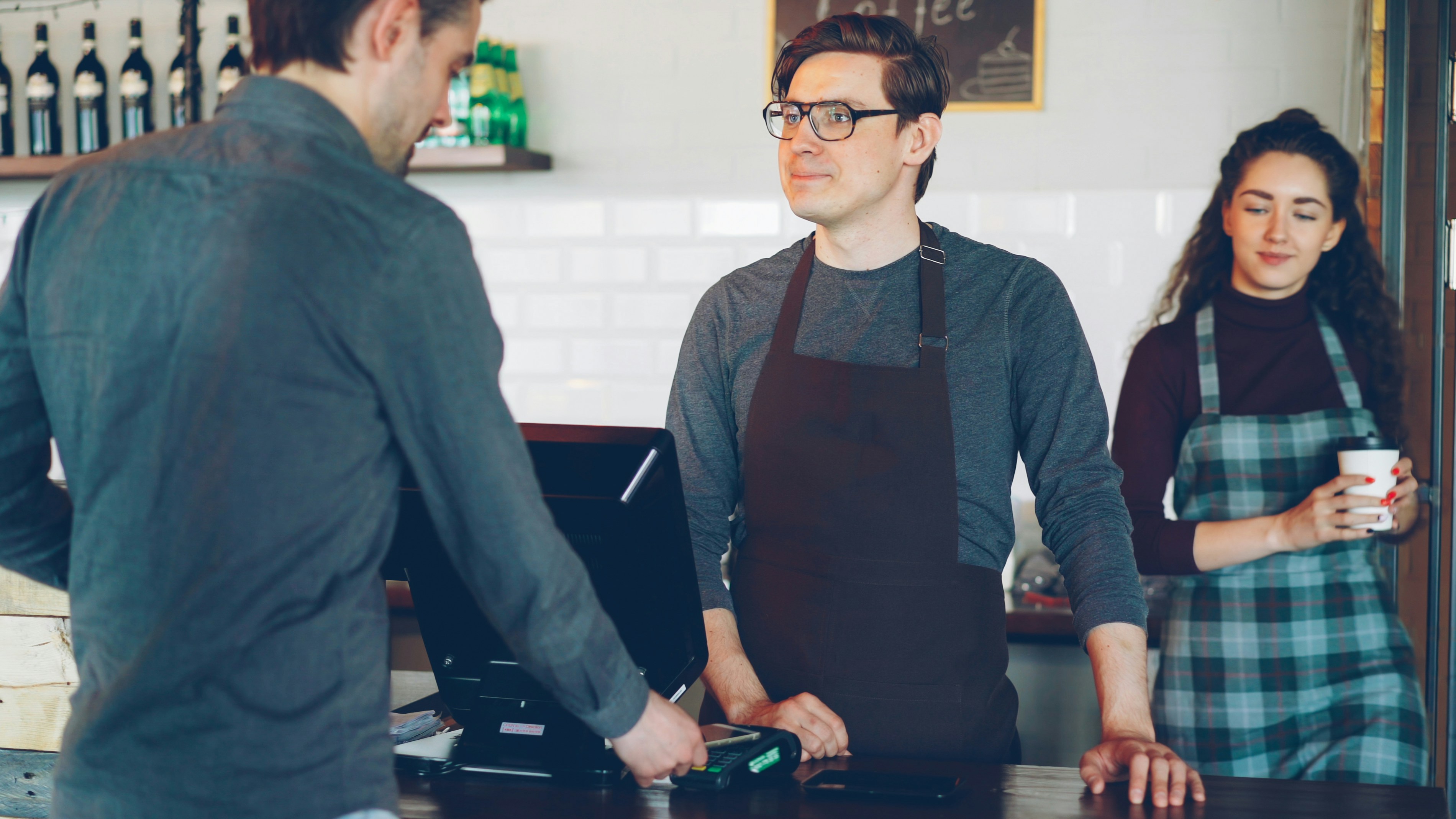 Barista with an apron talks with a customer while another barista watches.
